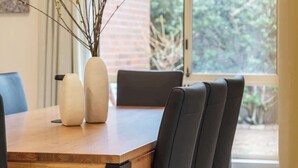 A dining area with a wooden table, black chairs, and a vase with branches. - Maison d'Art (Glenside)