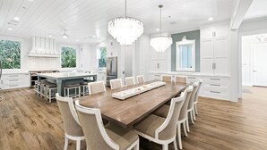 A spacious kitchen with a central island, white cabinetry, and a large dining table with chairs.