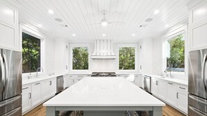 A modern kitchen with white cabinetry, a large island, stainless steel appliances, and a view of greenery outside.