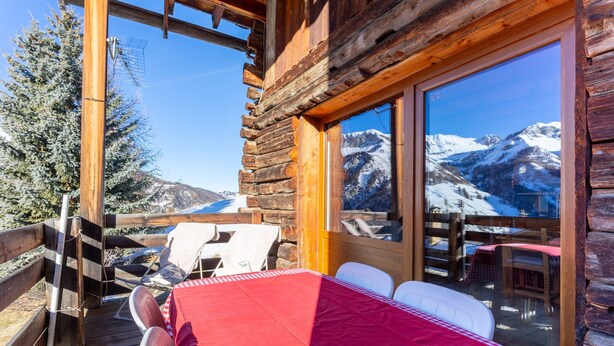 A wooden cabin with a dining table, chairs, and a view of snow-capped mountains. - Duplex Jouve with Exceptional View (Saint-Véran)