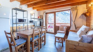 A wooden interior with a dining table, chairs, a sofa, a television, and a kitchen area with a microwave. - Duplex Jouve with Exceptional View (Saint-Véran)