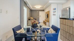 A modern living room with a glass coffee table, blue sofas, and a decorative vase. - Apt w/ BBQ Garage 550m From Beach Zuc0703 (Balneário Camboriú)