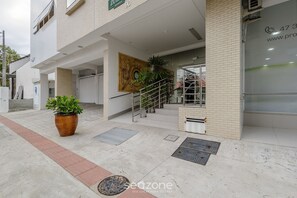 Entrada de un edificio con una escalera, una planta grande en maceta y un mural.