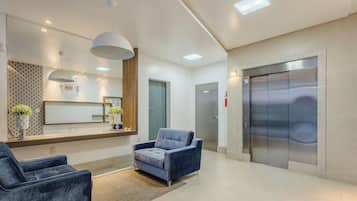 Un espace d’accueil moderne comprenant un comptoir de réception, deux coins salon, un grand miroir et un ascenseur.