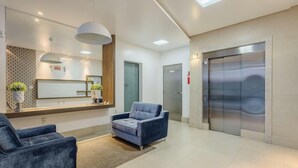 A reception area with a reception desk, two blue armchairs, a large mirror, and an elevator. - Apt w/ BBQ Garage 550m From Beach Zuc0703 (Balneário Camboriú)