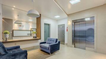 A modern reception area with a reception desk, two seating areas, a large mirror, and an elevator.
