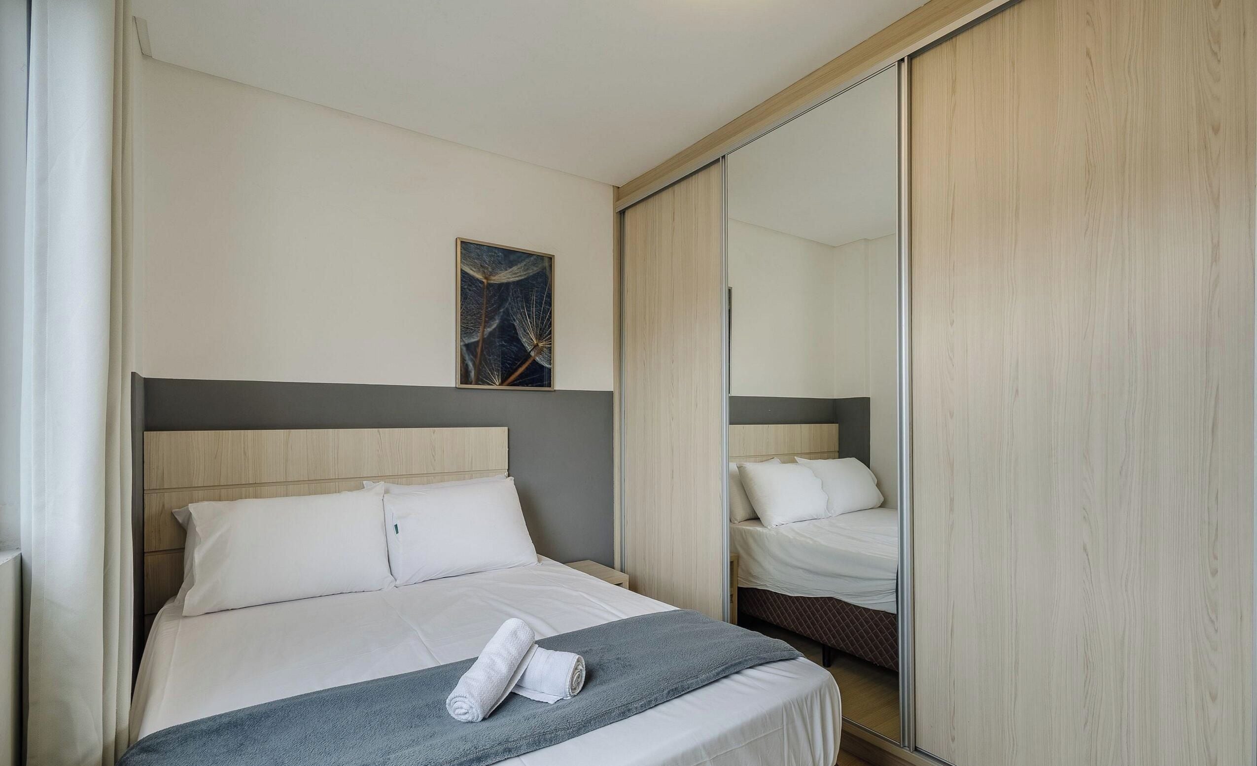 A hotel room with a bed, a mirror, and a painting on the wall.
