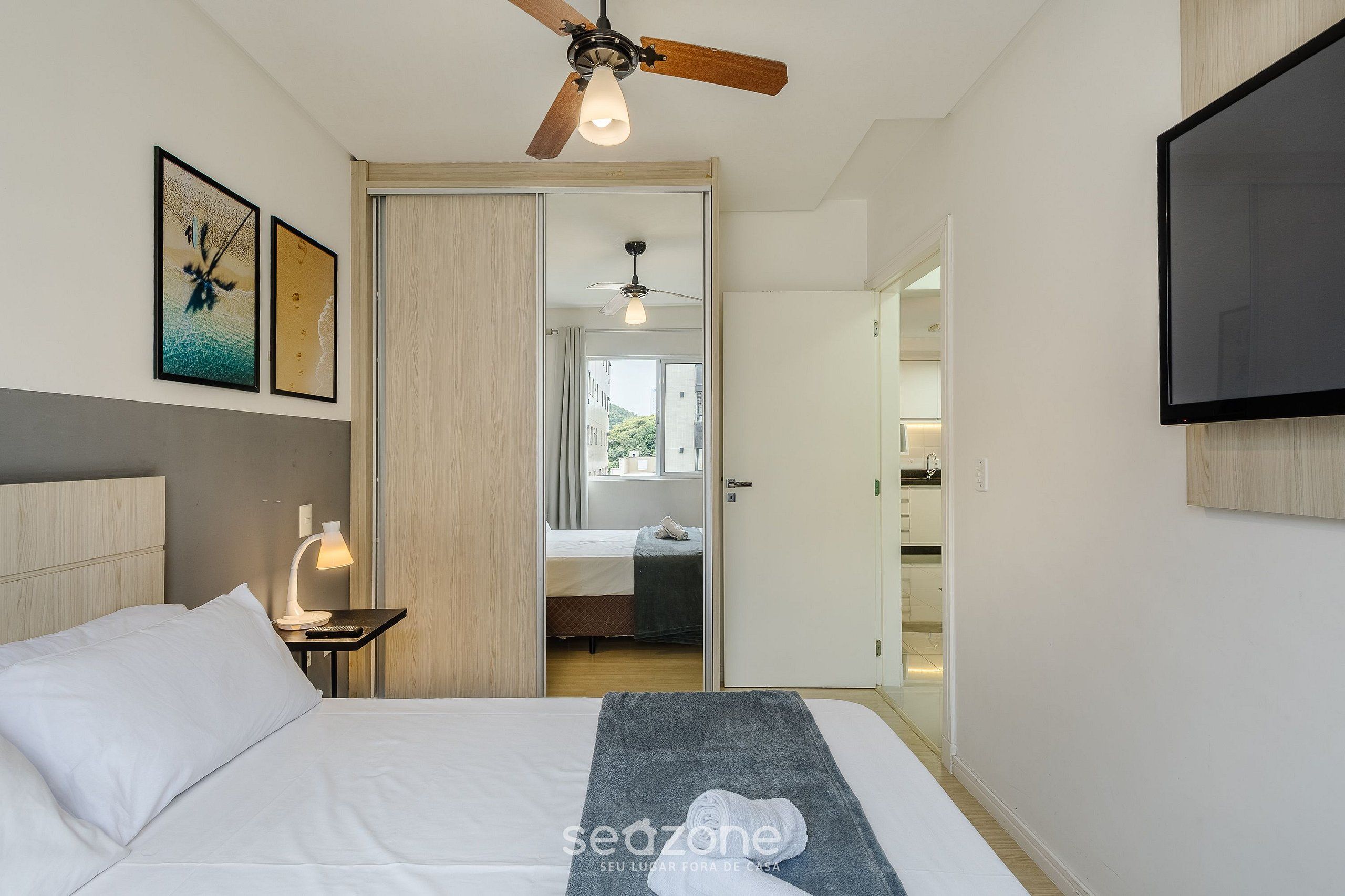 Quarto de hotel com cama, ventoinha no teto, televisão e obras de arte na parede.
