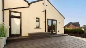 Una casa moderna de dos pisos con un porche de madera, una puerta principal y un ventanal pequeño.