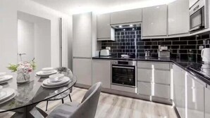Una cocina moderna con salpicadero negro, electrodomésticos de acero inoxidable y un comedor con mesa y sillas de vidrio.