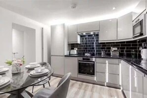 A modern kitchen with a black backsplash, stainless steel appliances, and a dining area with a glass table and chairs.
