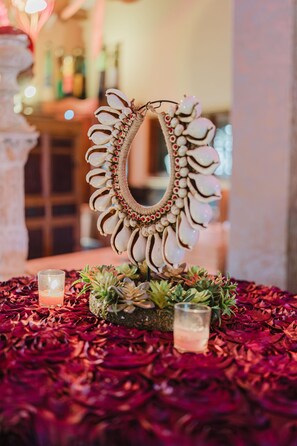 Un miroir décoratif orné de motifs floraux, entouré de pétales de roses rouges et agrémenté de deux bougies posées sur une table.