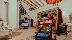 A traditional room with a wooden bed, a blue sofa, and a chandelier. - House of Mosaic Aruba - Unique Experience (Oranjestad)
