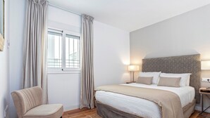 A bedroom with a bed, a chair, a window with curtains, and a bedside table with a lamp. - Lovely Apartment in the Center. San Antonio III (Cádiz)