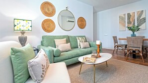 A living room with a green sofa, a round coffee table, and a dining area with wicker chairs. - Lovely Apartment in the Center. San Antonio III (Cádiz)