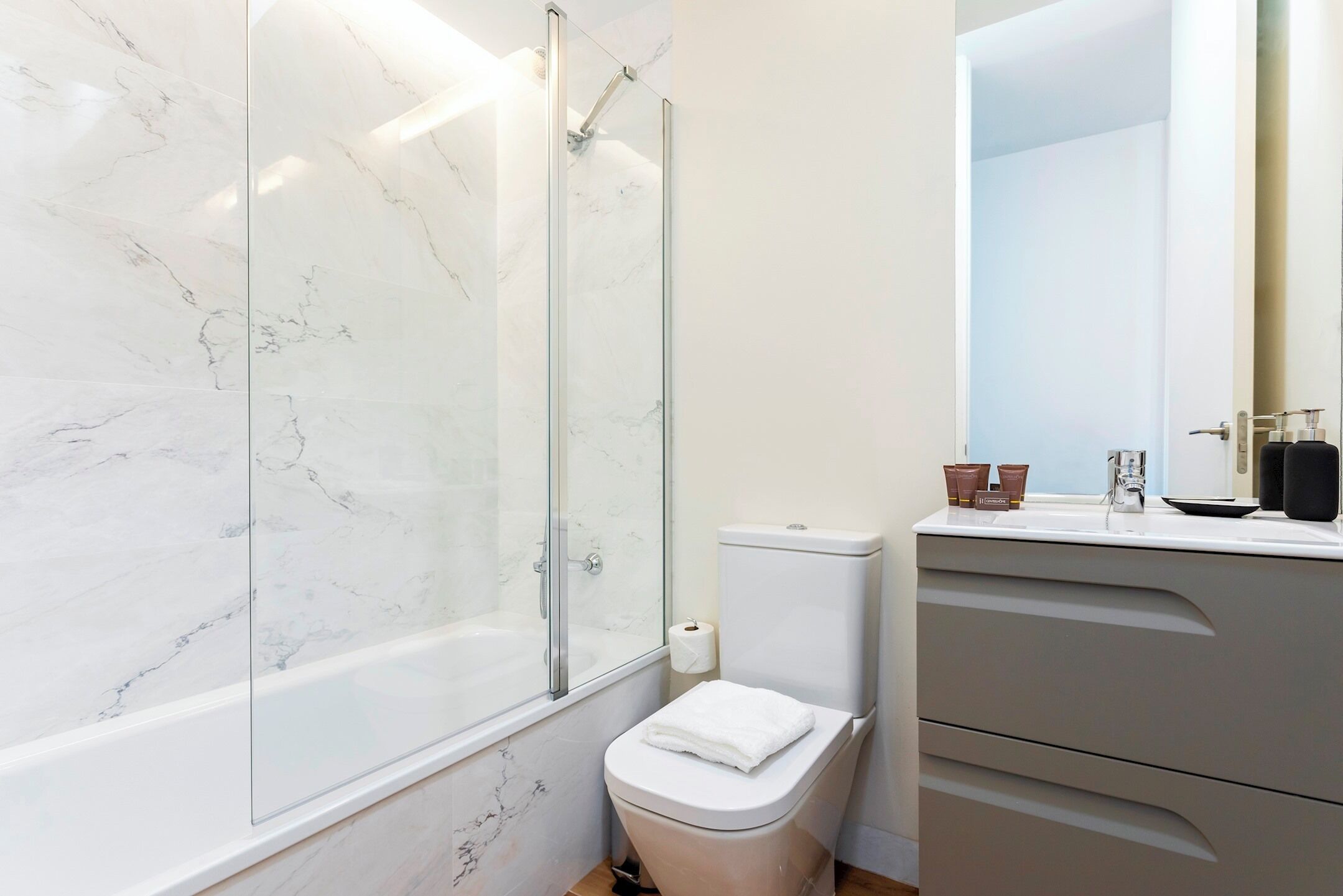 A bathroom with a glass-enclosed shower, a toilet, and a vanity with a mirror.