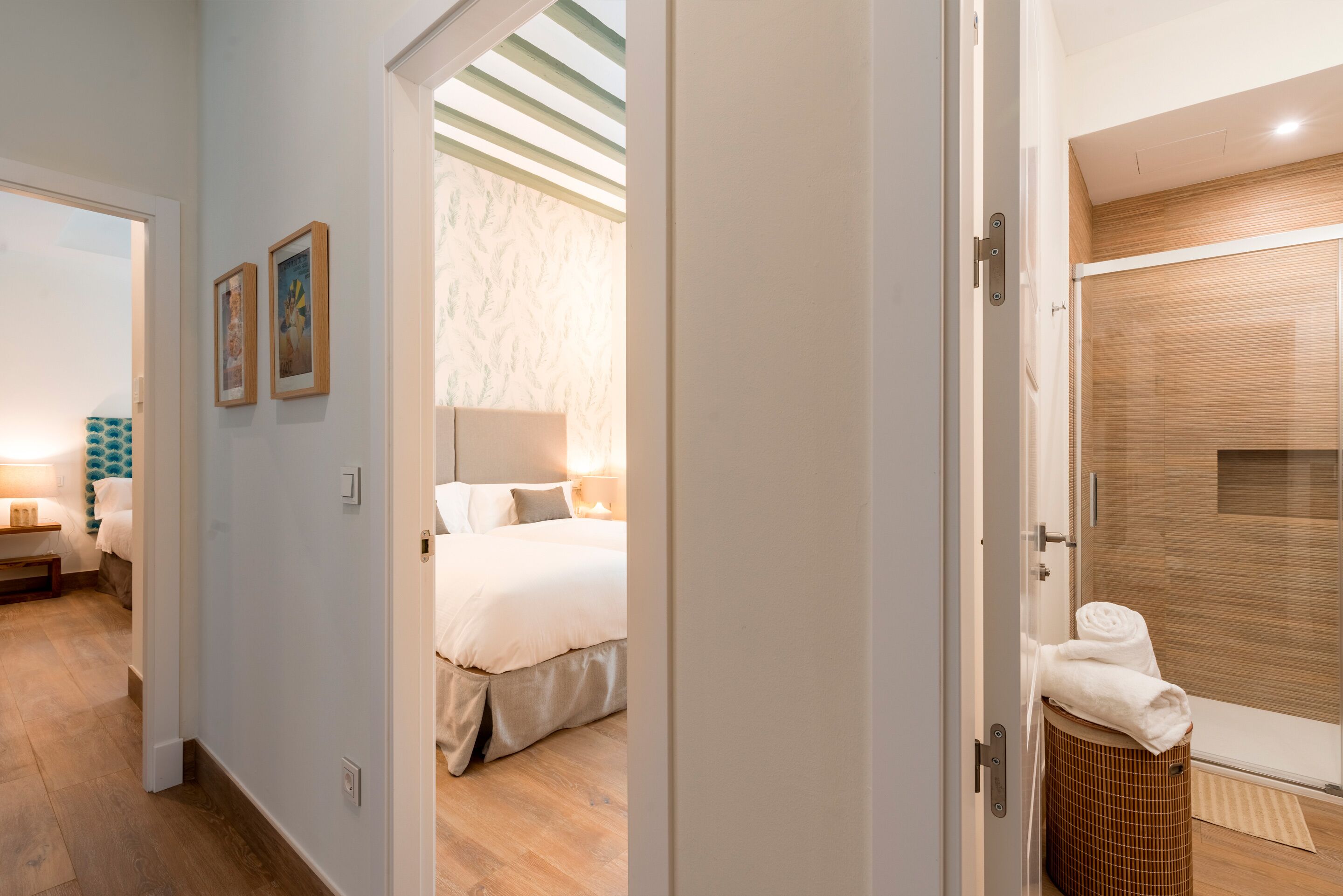 Una habitación de hotel con cama, baño con ducha y pasillo con puerta que da a otra habitación.