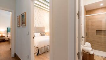 Una habitación de hotel con cama, baño con ducha y pasillo con puerta que da a otra habitación.