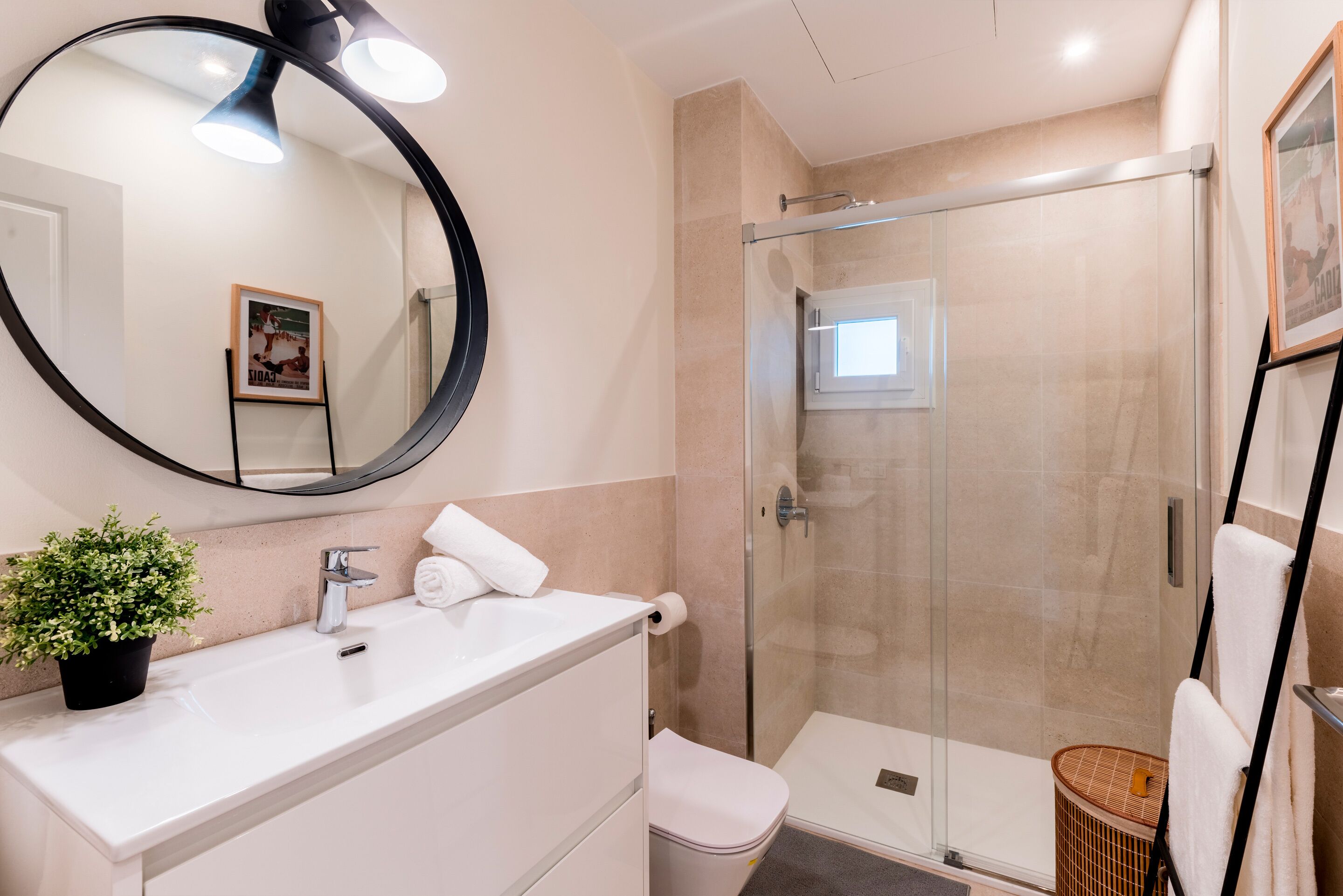 A modern bathroom with a round mirror, a sink, a toilet, and a glass-enclosed shower.