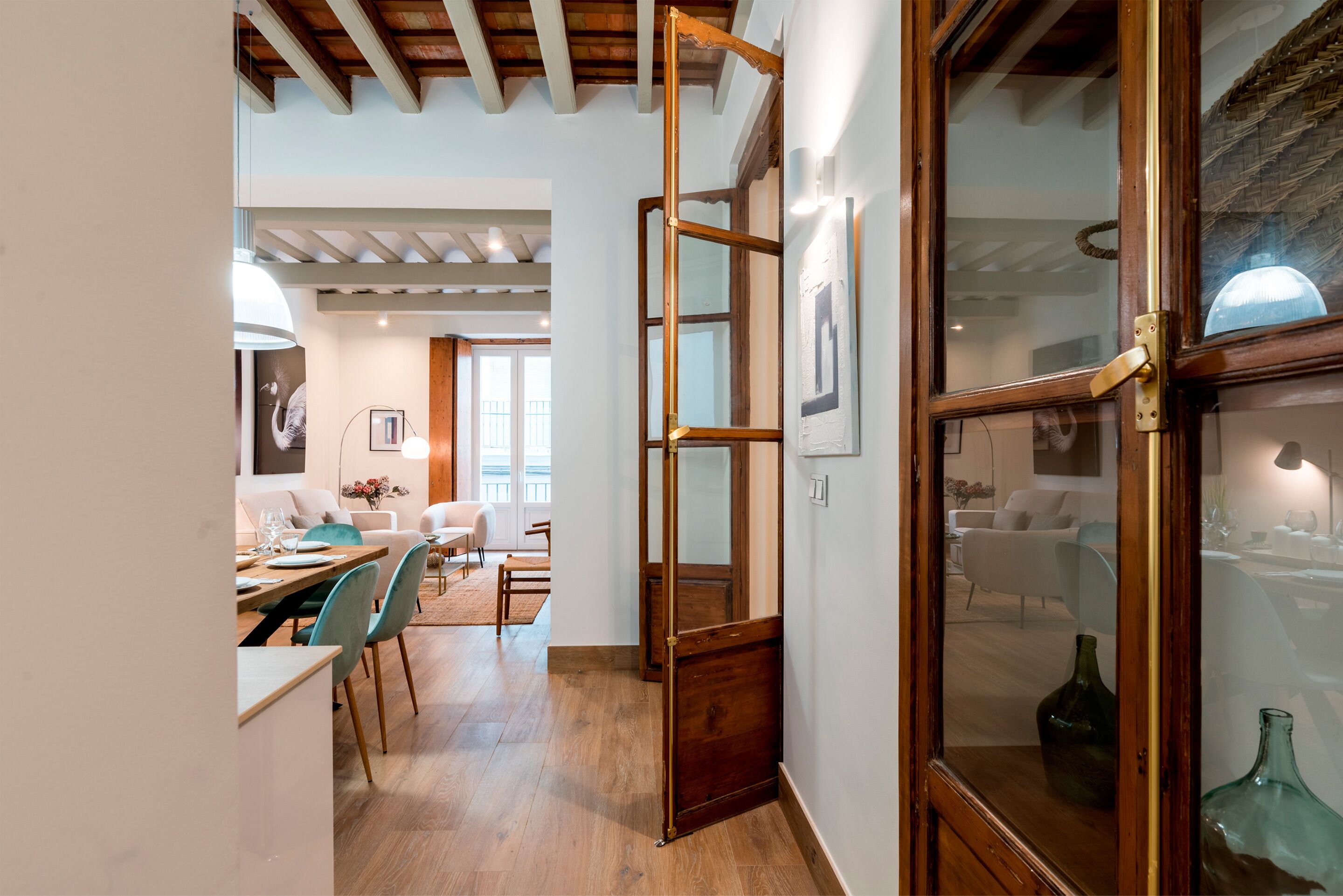 A modern interior with a wooden floor, a dining area with chairs and a table, and a large window with a view.