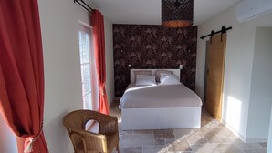 Ein Schlafzimmer mit Bett, einem Korbstuhl, einem Kleiderschrank und einem Fenster mit Vorhängen.