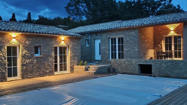Ein Steinhaus mit überdachter Terrasse und Poolbereich.