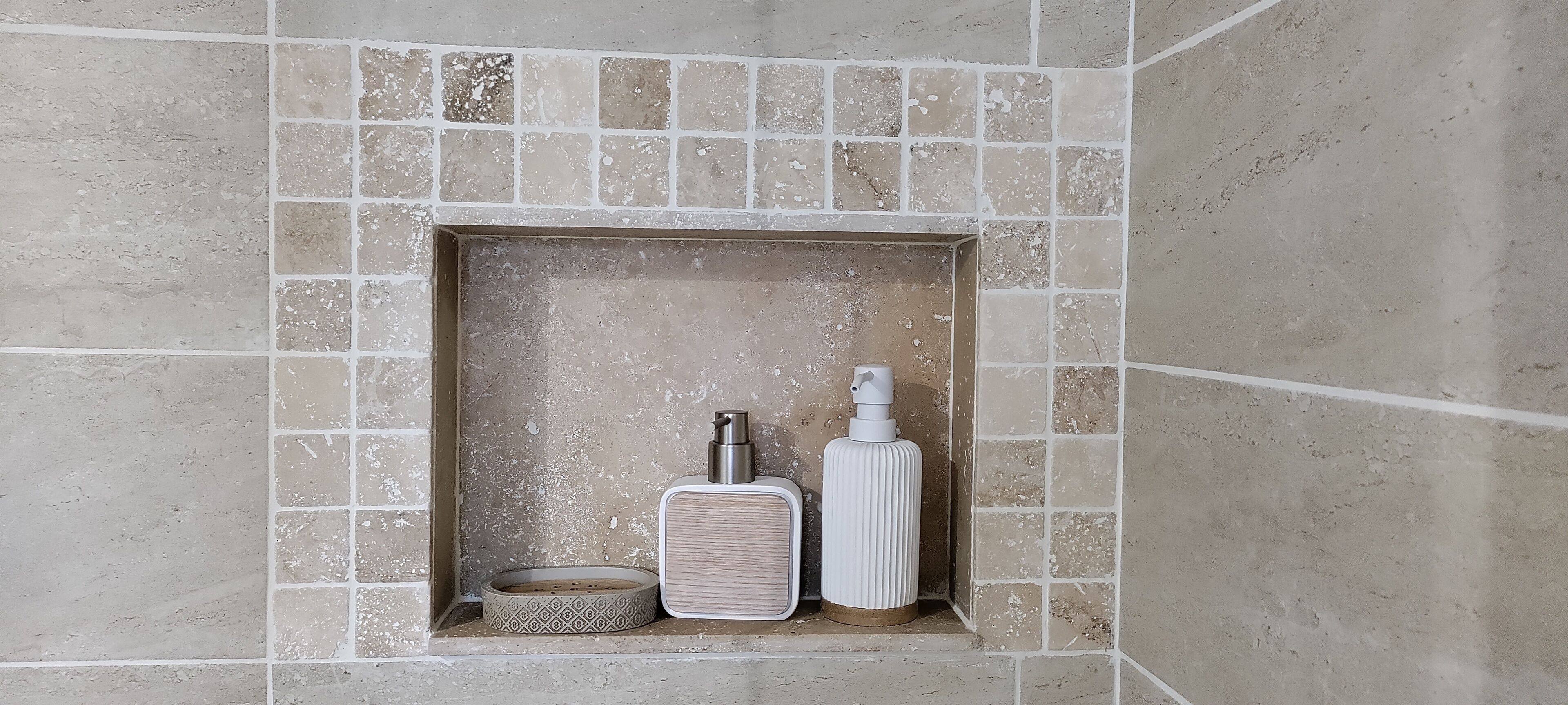 A bathroom with a tiled wall, a rectangular shelf with a bottle and a soap dish.