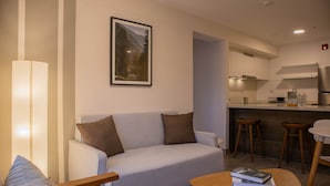 Et moderne hotelværelse med sofa, et lille bord med bøger, et tekøkken og et billede i ramme på væggen.