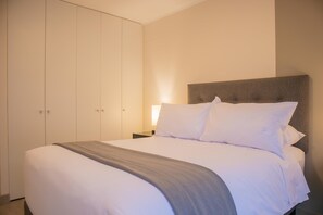 A neatly made bed with a grey throw blanket, a headboard, and white bedding.