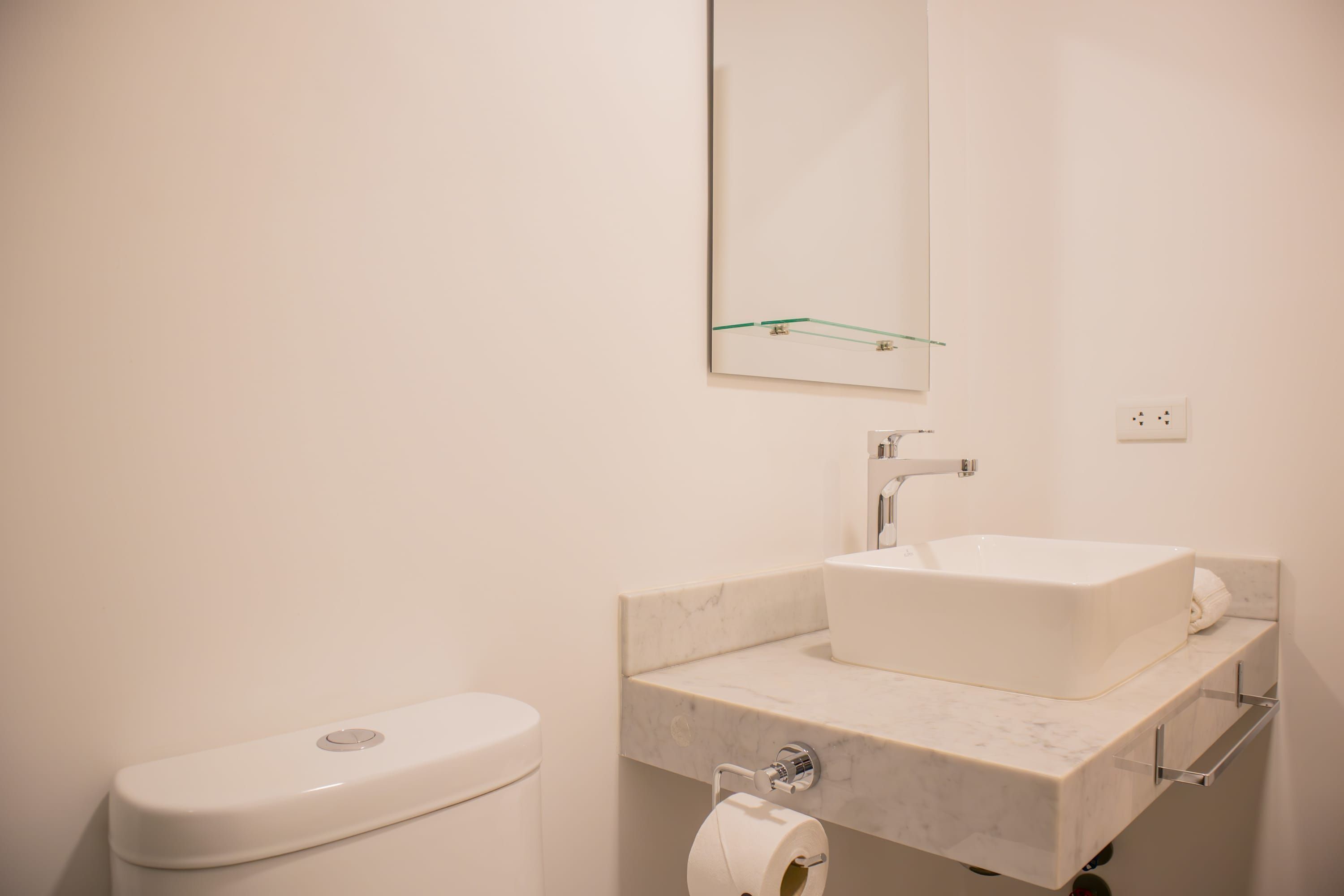 Ein modernes Badezimmer mit Toilette, Marmorwaschbecken und einer Glasablage.