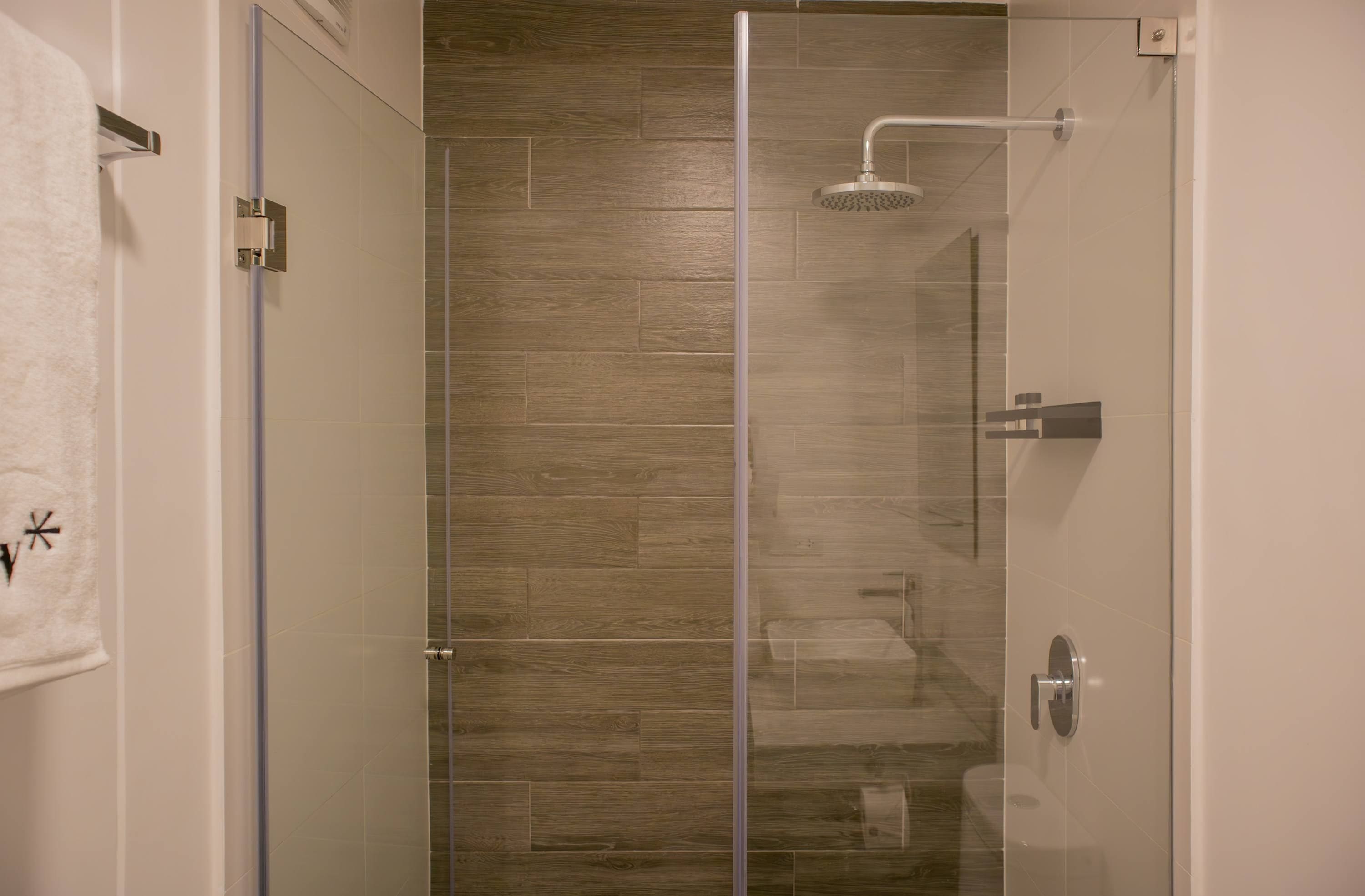 Une douche moderne avec une porte en verre, un sol en bois et un porte-serviettes apparent.