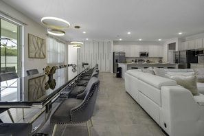 Een moderne keuken met witte kastjes, roestvrijstalen apparatuur en een eethoek met een lange tafel en stoelen.