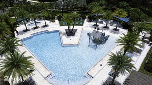 Una piscina amplia y cristalina rodeada de palmeras y tumbonas, con una zona de juegos acuáticos cerca.