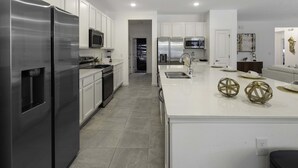A modern kitchen with stainless steel appliances, white cabinetry, and a central island with decorative spheres. - Family Villa w Pool Games n Themed Rooms (Kissimmee)