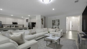 A modern living room with a sectional sofa, a coffee table, and a kitchen in the background. - Family Villa w Pool Games n Themed Rooms (Kissimmee)