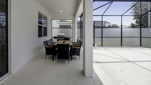 A modern outdoor dining area with a table and chairs, a grill, and a view of the surrounding landscape. - Family Villa w Pool Games n Themed Rooms (Kissimmee)