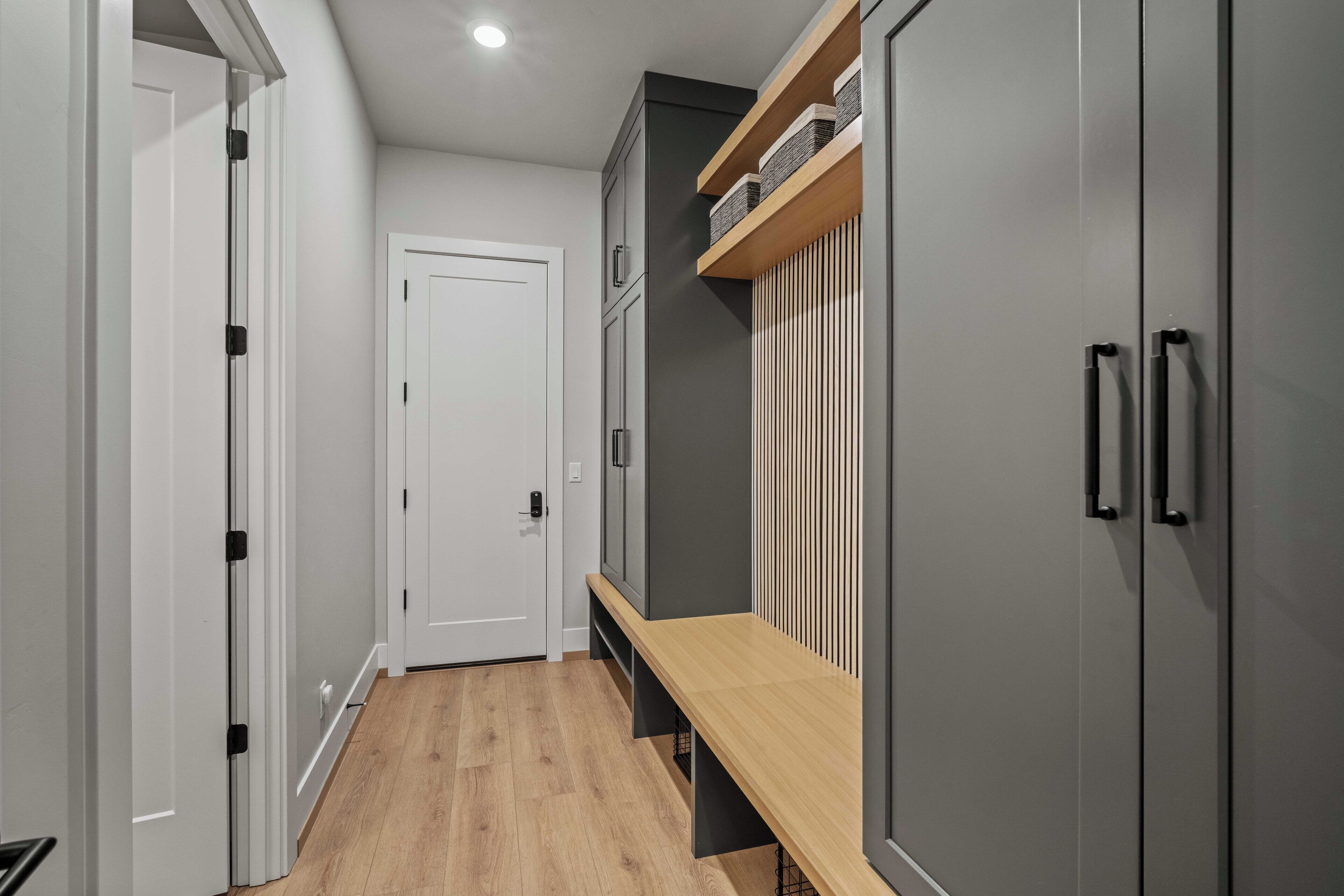 A hallway with a bench, grey cabinets, and a white door.