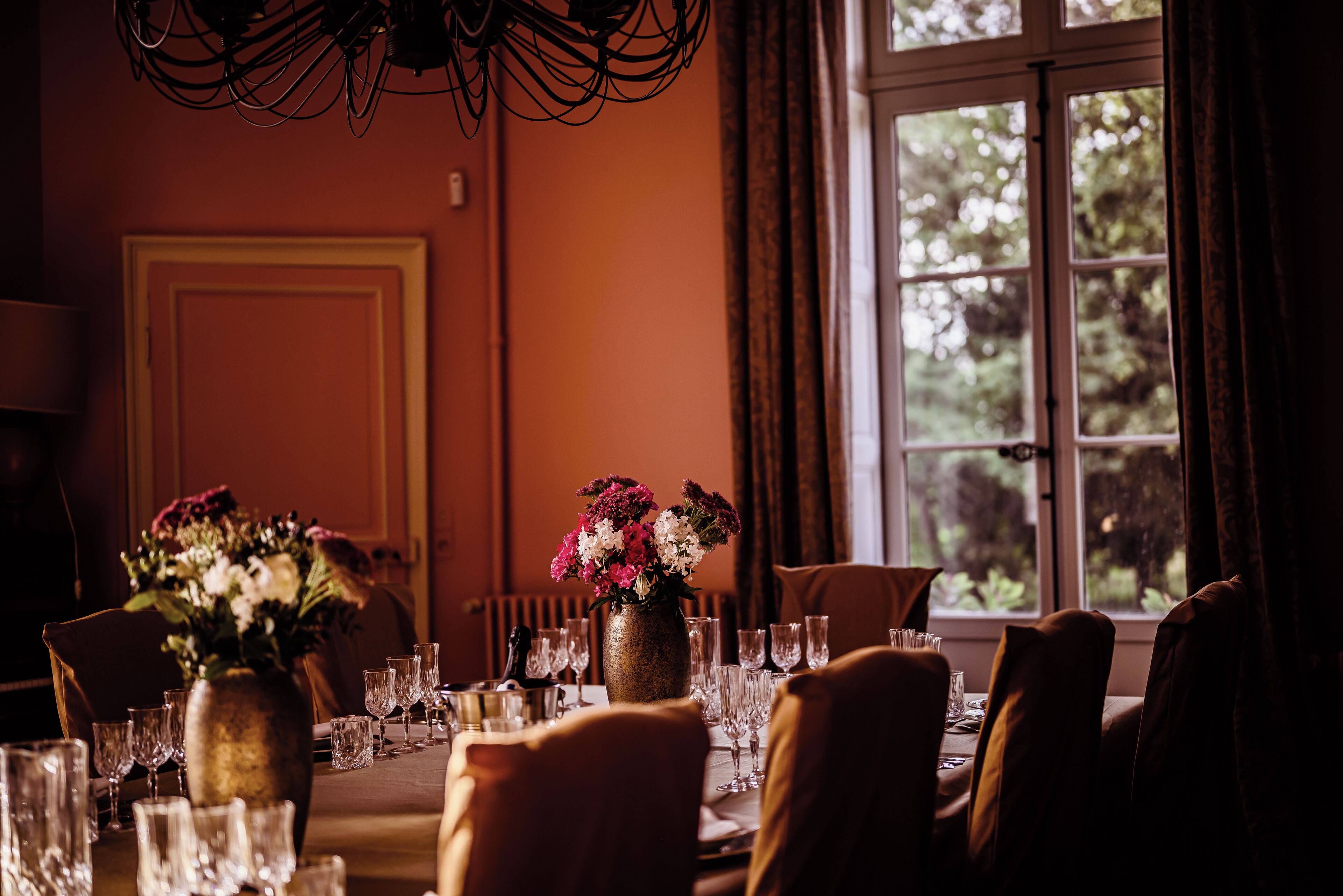 Comedor con una mesa dispuesta para una comida, un florero y una ventana con cortinas.