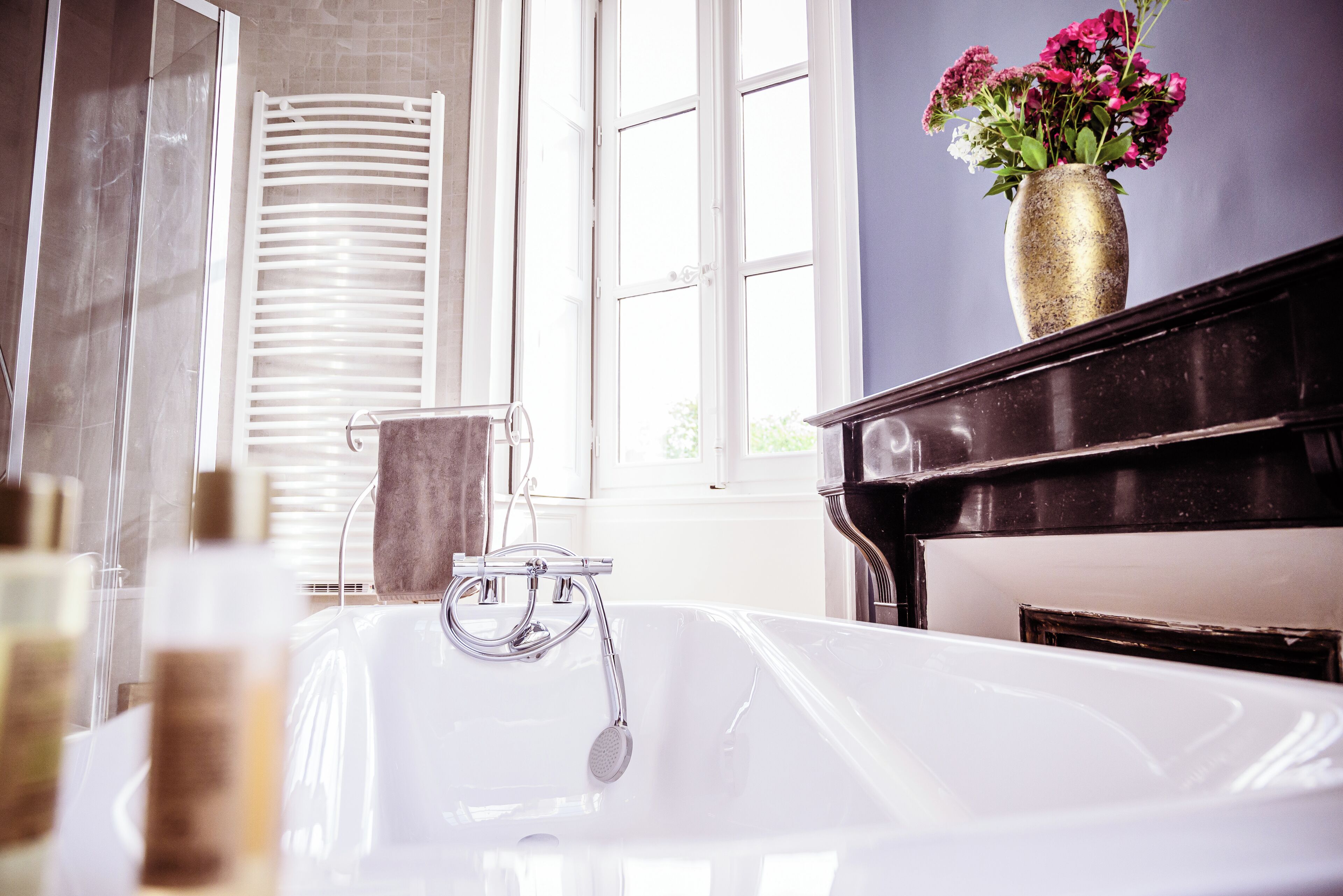 A bathroom with a bathtub, a towel rack, and a vase with flowers on a piano.
