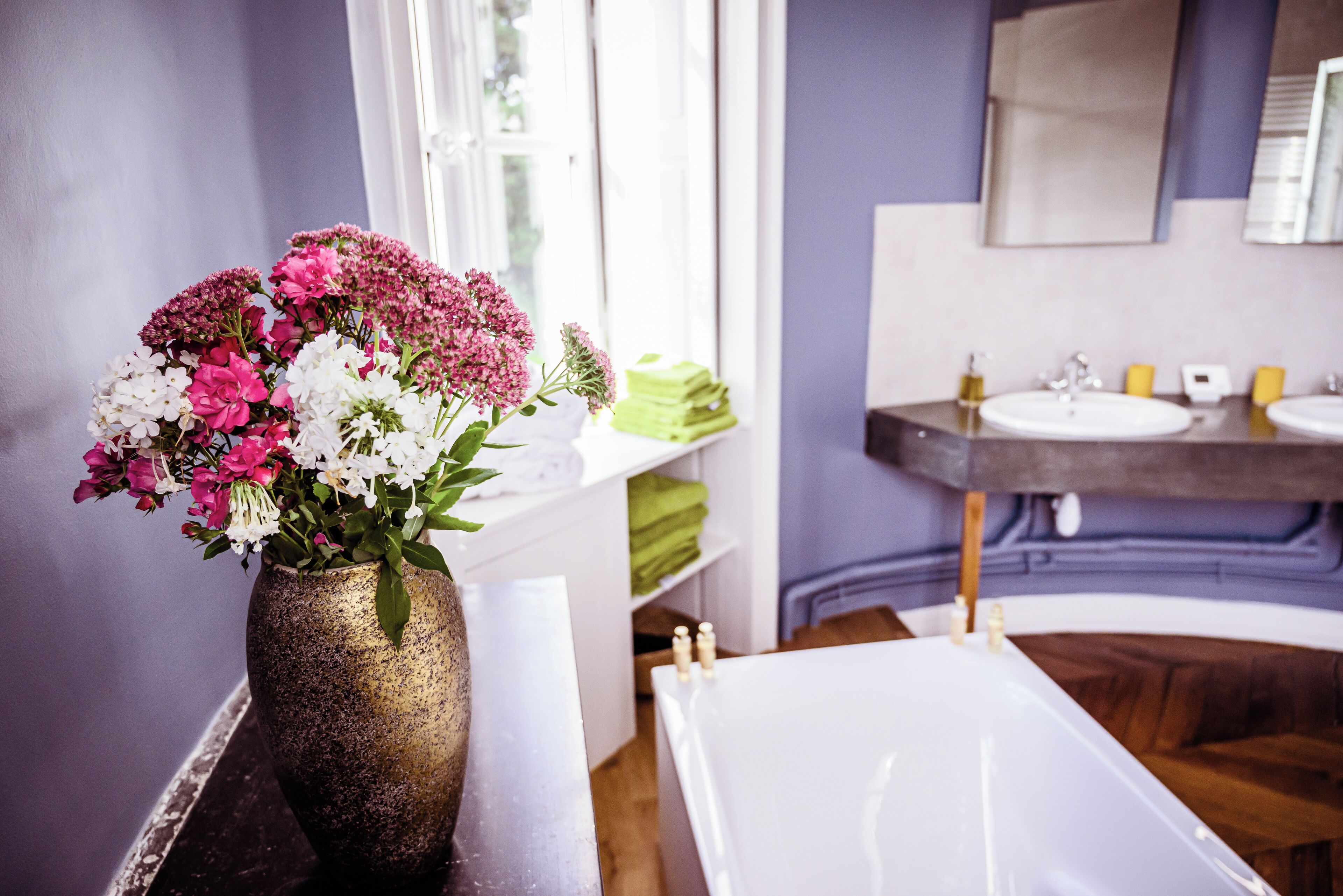 A bathroom with a bathtub, a sink, and a vase of flowers on a shelf.