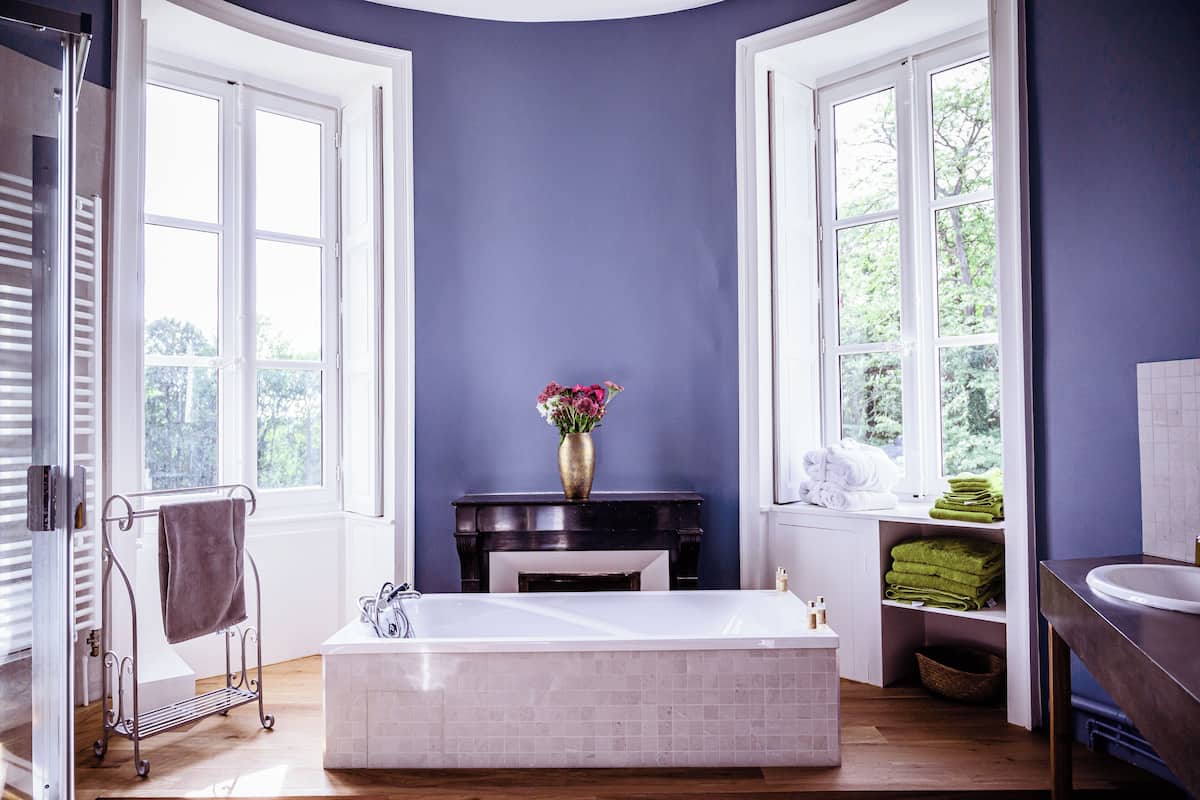 Un baño con bañera, tocador con lavabo, un florero con flores y toallas en estantes.