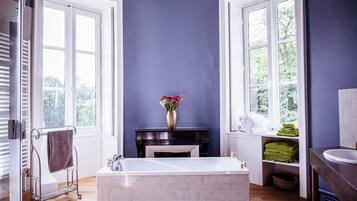 A bathroom with a bathtub, a vanity with a sink, a vase with flowers, and towels on shelves.