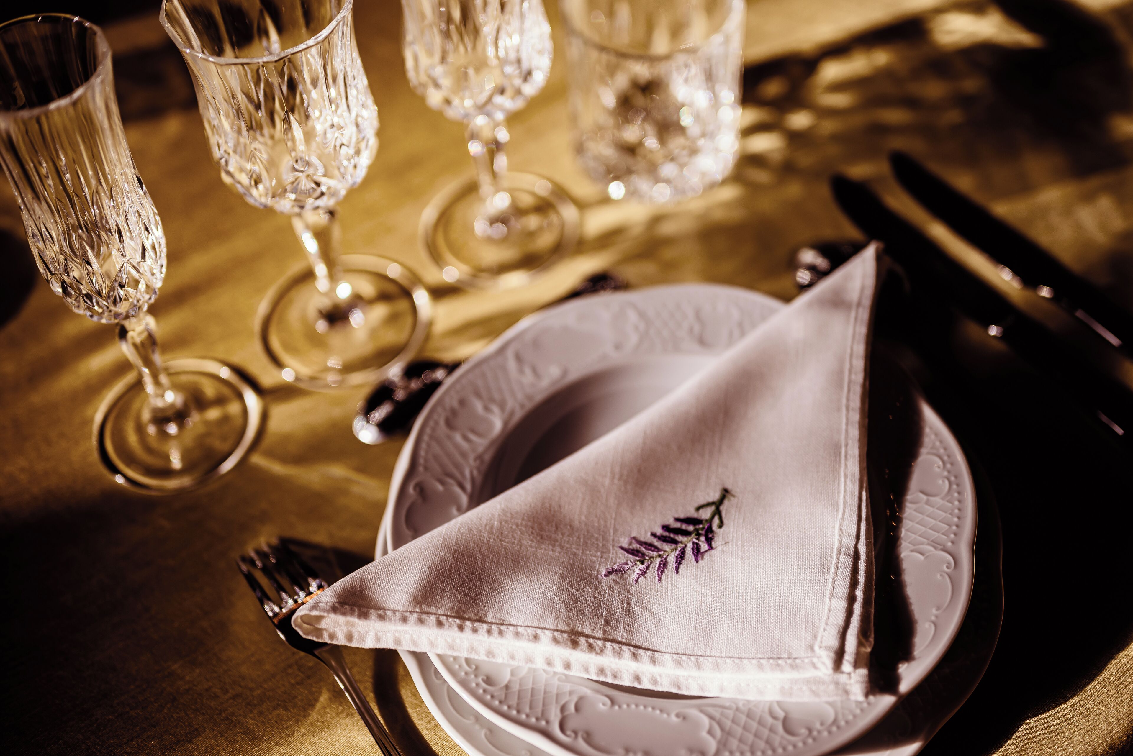 A table setting with a folded napkin, a fork, a knife, and three crystal glasses.