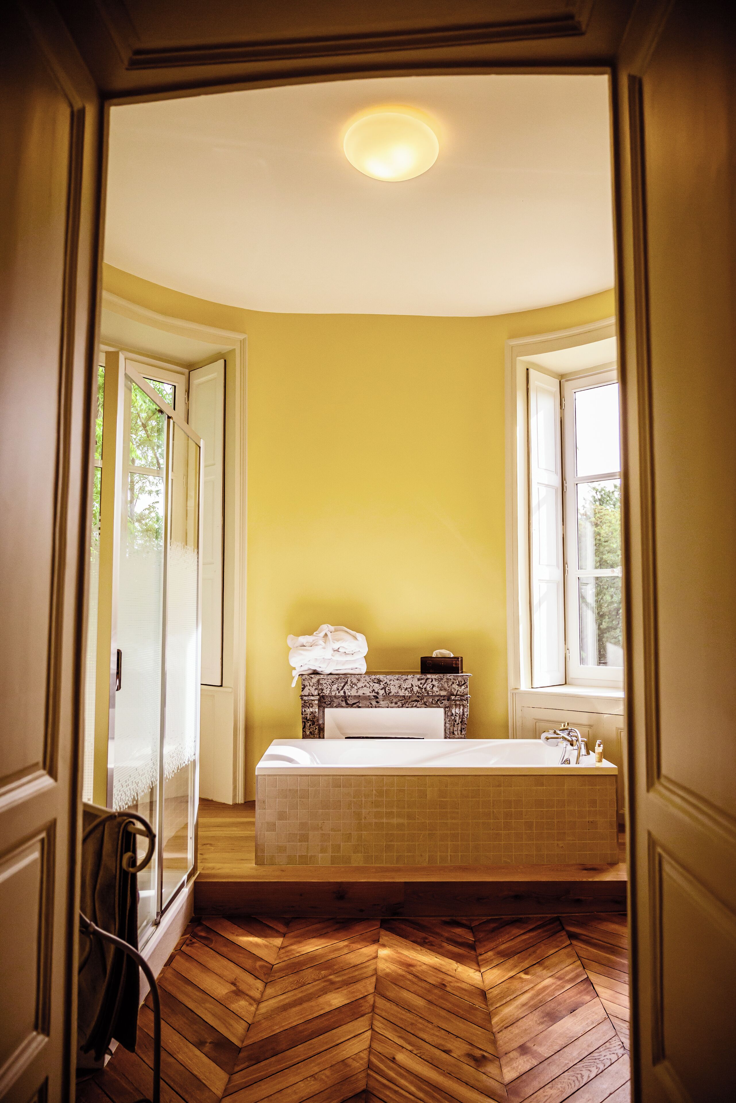 A bathroom with a herringbone floor, a bathtub, and a window providing natural light.