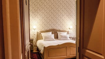 Ein Hotelzimmer mit Holzboden, einem Bett mit weißen Laken und Wandpapier mit Muster.