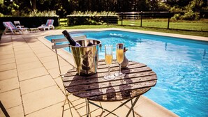 A poolside setting with a wooden table, a metal bucket, and two glasses of champagne. - Château de la Grange Moreau (Vallon-sur-Gée)