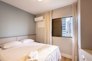 A hotel room with a bed, a window with blinds, an air conditioning unit, and a view of buildings outside. - 3br Apt Sea View BBQ Garage - BC Vld1002 (Balneário Camboriú)