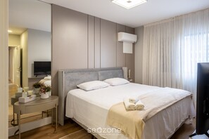 A modern hotel room with a large bed, a bedside table with a lamp, a flat-screen TV, and a window with curtains. - 3br Apt Sea View BBQ Garage - BC Vld1002 (Balneário Camboriú)