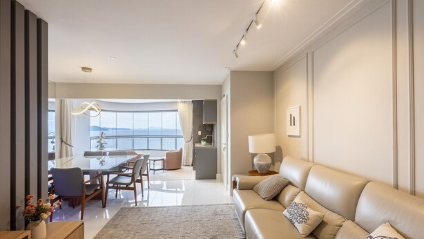 Una sala de estar moderna con un sofá, un comedor con mesa y sillas, y vista al mar a través de amplios ventanales.