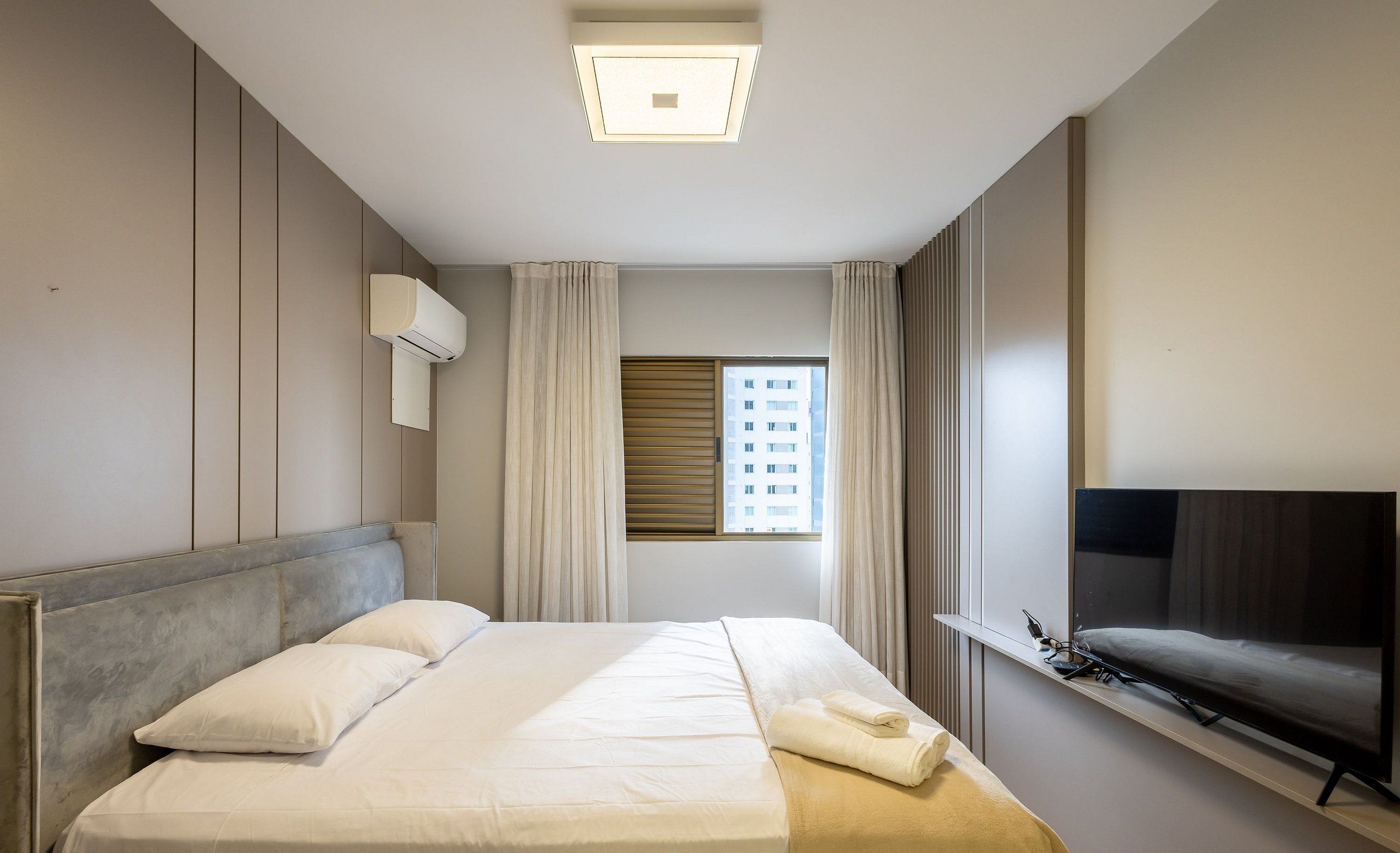 Una habitación de hotel moderna con una cama grande, un televisor de pantalla plana y una ventana con persianas.